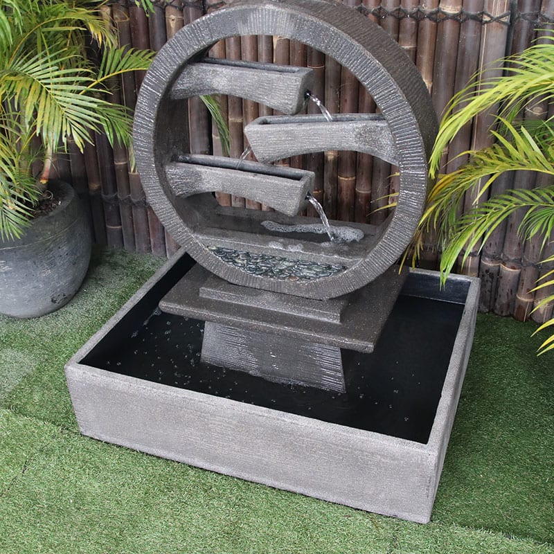 Galleria Imports Wagon Wheel Fountain medium grey top right angle view with greenery