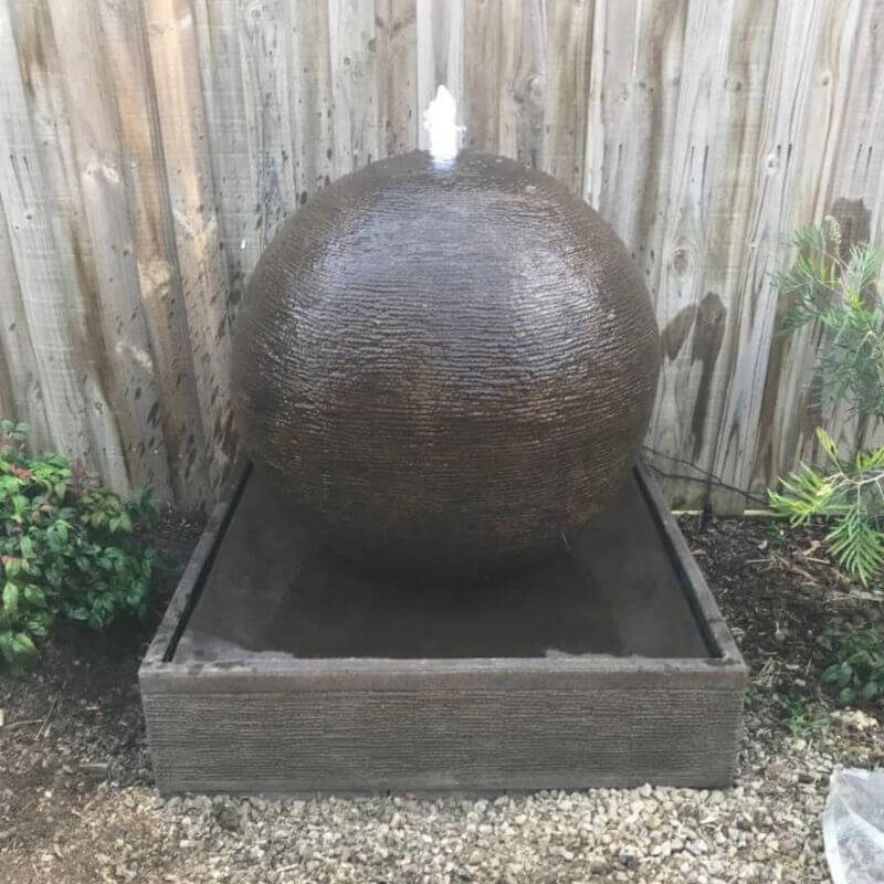 Luna Ball Fountain Small in Rust with wooden fence in the background