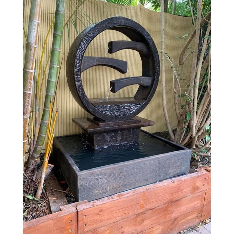 Wagon Wheel Fountain Large Charcoal with bamboo trees surround closeup